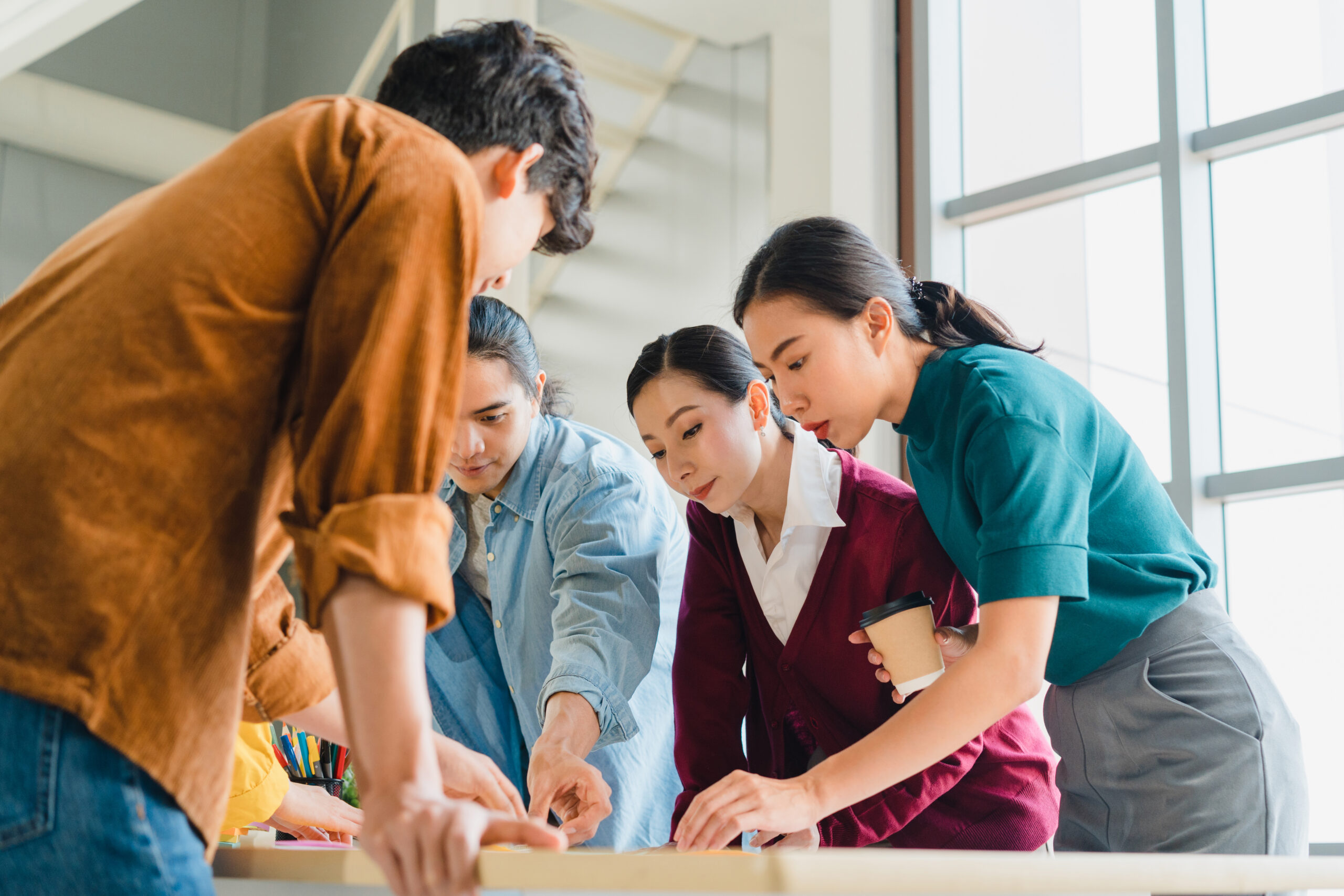 Asian businessmen and businesswomen meeting brainstorming ideas about creative web design planning application and developing template layout for mobile phone project working together in small office.